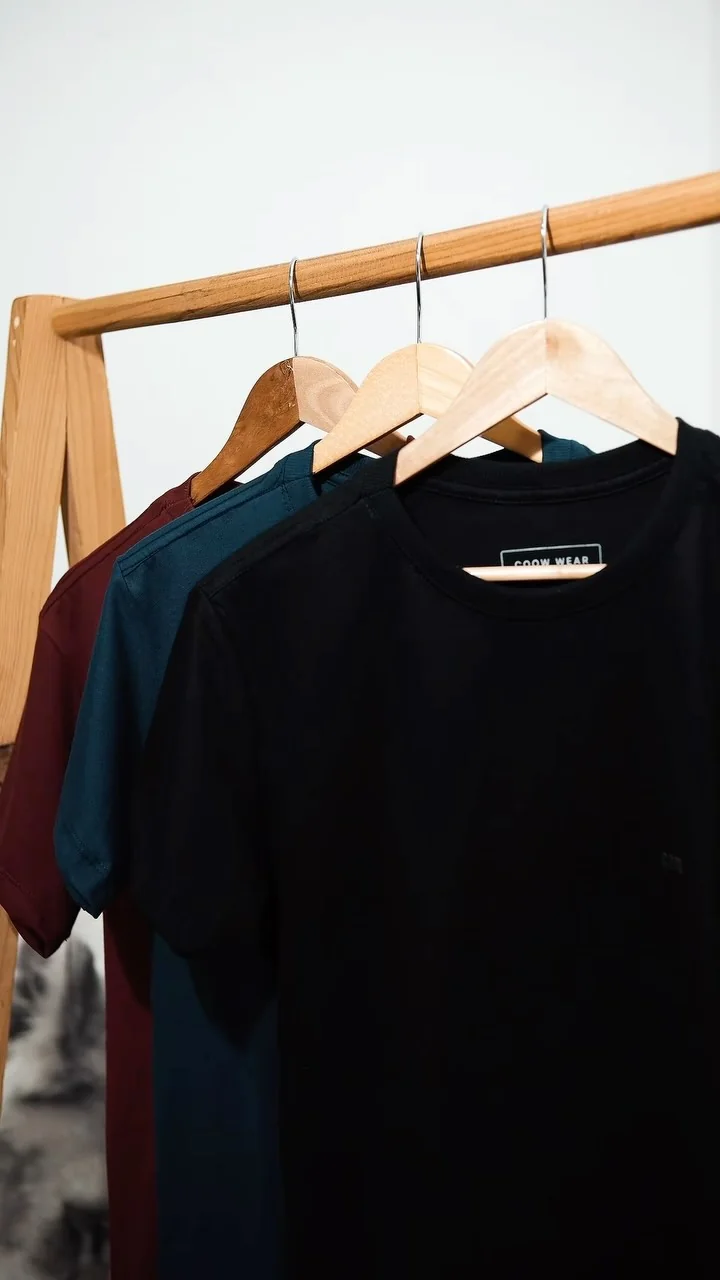 Camisetas COOW WEAR em cabideiro de madeira com destaque para gola e corte estruturado